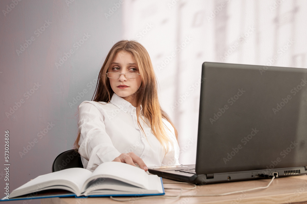 The girl is sitting at the table and looking at the laptop. The girl is sitting at the table and looking at the laptop.