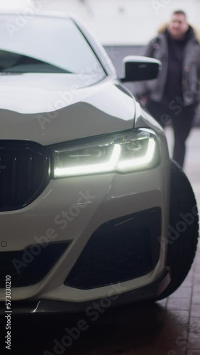 Vertical video. A white passenger car slowly turns in front of the camera. You can see the left front side of the car, headlight, bumper, radiator, wheel. Visit to the maintenance service.