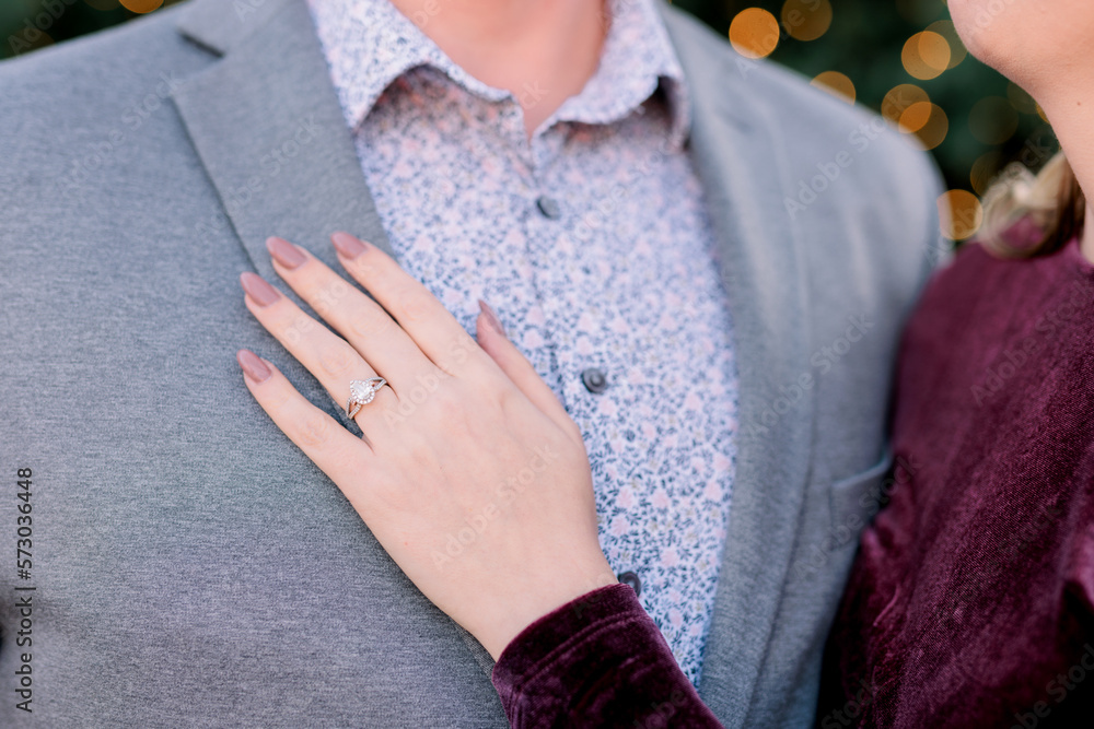 A woman's young hand is touching a young man wearing a flower blue dress shirt and gray blazer showing off her engagement ring. A woman's young hand is touching a young man wearing a flower blue dress shirt and gray blazer showing off her engagement ring.