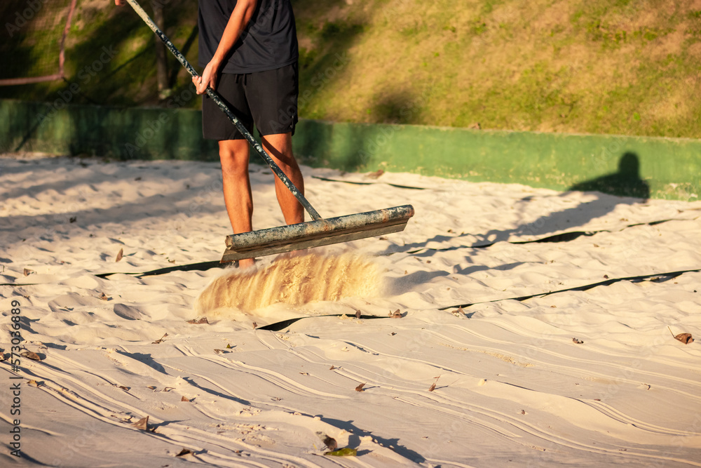 Foto de Sand beach tennis level. Sand cleaning with rake. Man working