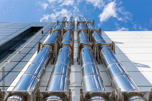 Foto Chrome ventilation pipes on the outer wall of a black-and-white industrial building against a blue sky background