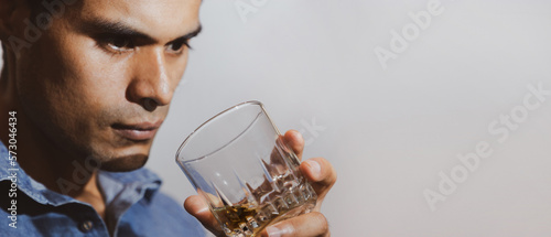 Fotografiet hombre joven triste y mirando con bebida en su mano en un fondo gris y espacio para texto, concepto de problemas con las bebidas alcohólicas, depresión, alcoholismo