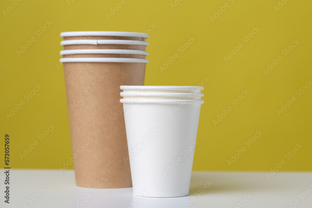 Disposable cardboard biodegradable glass on a white table, yellow background. Disposable cardboard biodegradable glass on a white table, yellow background.