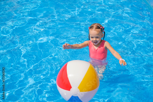 The baby is running after an inflatable ball on water in the pool.