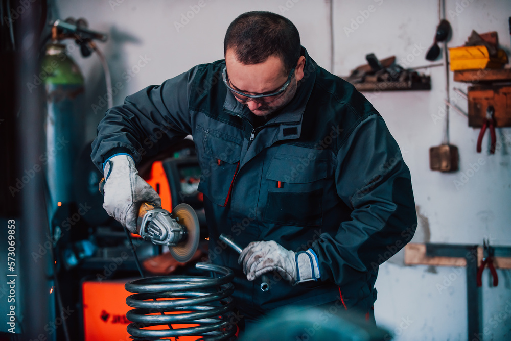 Fototapeta premium Locksmith in special clothes and goggles works in production. Metal processing with angle grinder. Sparks in metalworking.