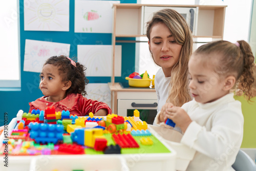 Teacher with girls playing with construction blocks sitting on table at kindergarten