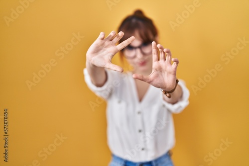Young beautiful woman wearing casual shirt over yellow background doing frame using hands palms and fingers, camera perspective
