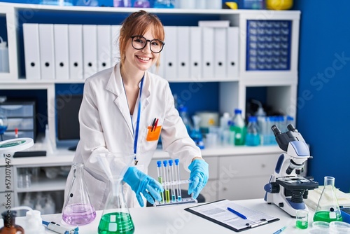 Young woman scientist smiling confident holding test tubes at laboratory