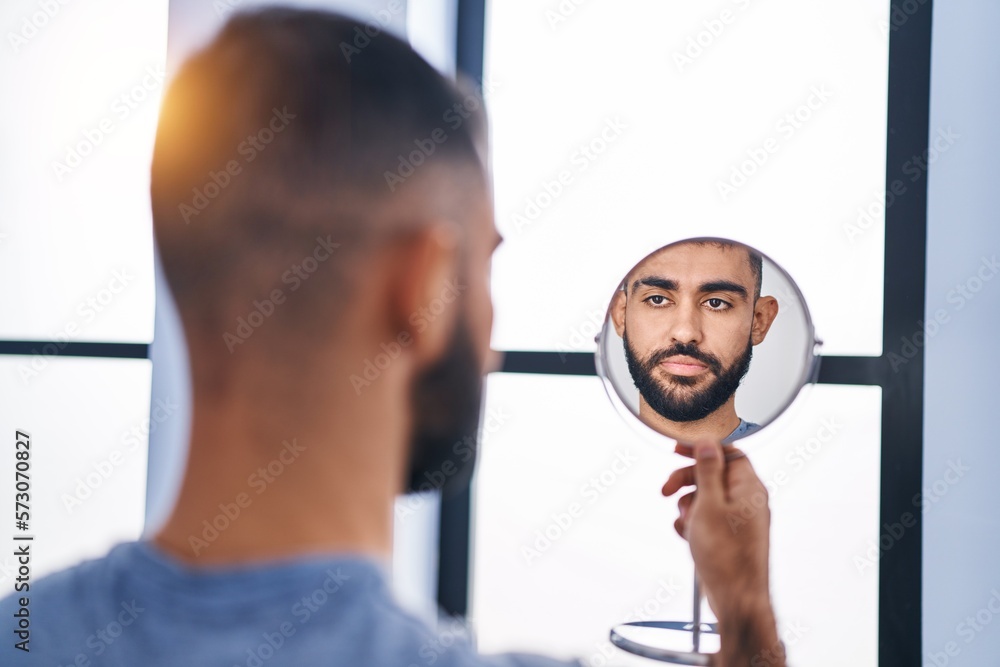 Young hispanic man looking face on mirror at home Young hispanic man looking face on mirror at home
