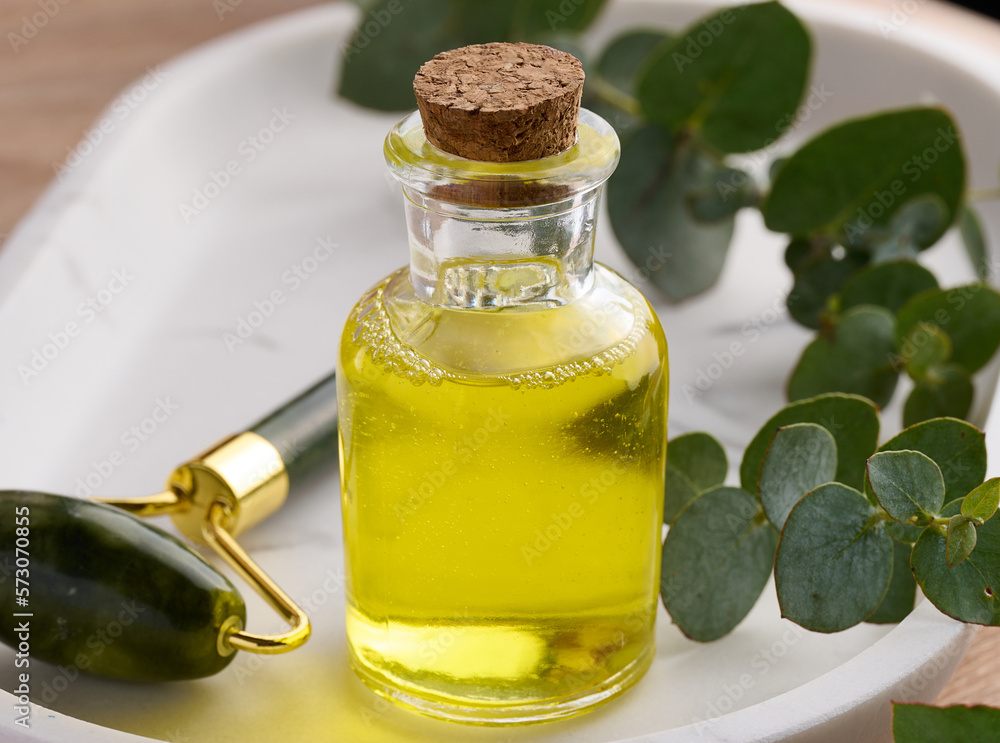Transparent glass bottle with yellow oil and eucalyptus branch, cosmetic product Transparent glass bottle with yellow oil and eucalyptus branch, cosmetic product