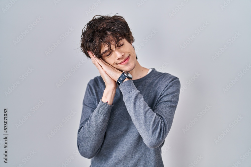Young man standing over isolated background sleeping tired dreaming and posing with hands together while smiling with closed eyes. Young man standing over isolated background sleeping tired dreaming and posing with hands together while smiling with closed eyes.