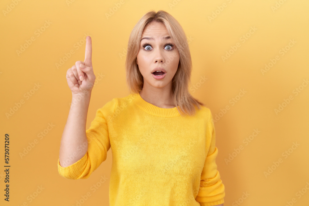 Young caucasian woman wearing yellow sweater pointing finger up with successful idea. exited and happy. number one. Young caucasian woman wearing yellow sweater pointing finger up with successful idea. exited and happy. number one.