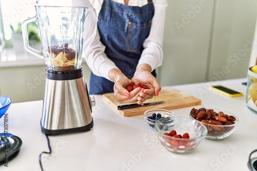 Young blonde woman holding raspberries at kitchen