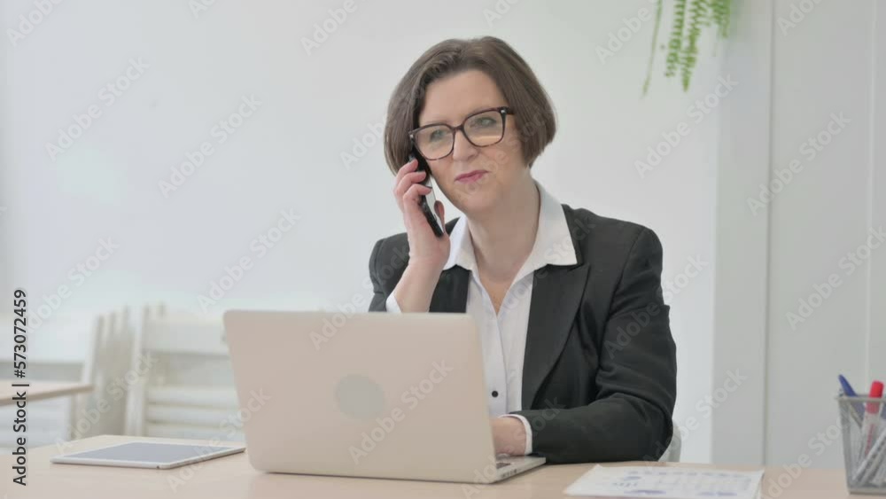 Old Businesswoman Talking on Phone while using Laptop Old Businesswoman Talking on Phone while using Laptop
