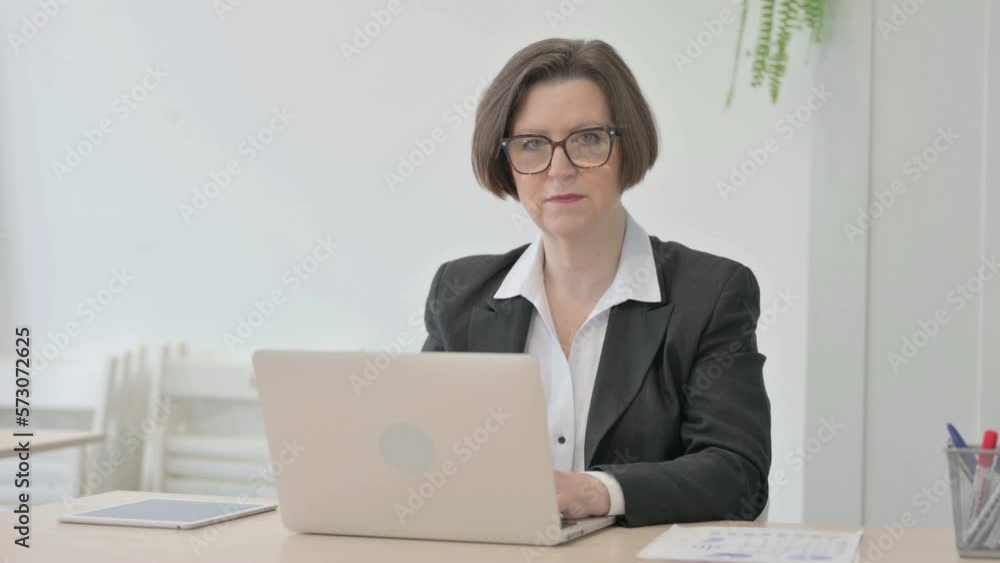 Old Businesswoman Looking at Camera while using Laptop Old Businesswoman Looking at Camera while using Laptop