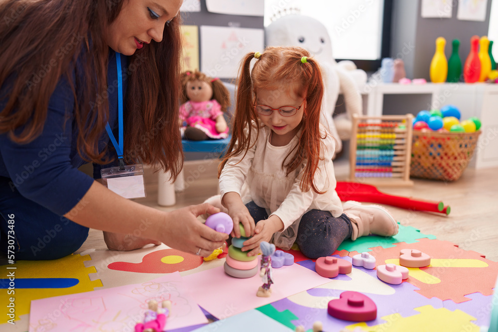 Fototapeta premium Teacher and student playing with hoops toys sitting on floor at kindergarten