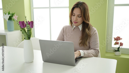 Young beautiful hispanic woman using laptop sitting on table at home