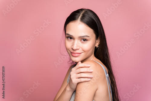 Young woman touching her shoulder on pink background in studio