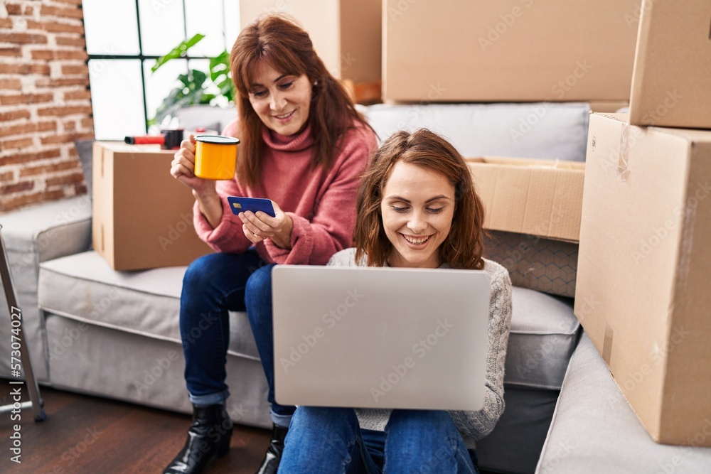 Two women mother and daughter using laptop and credit card drinking coffee at new home