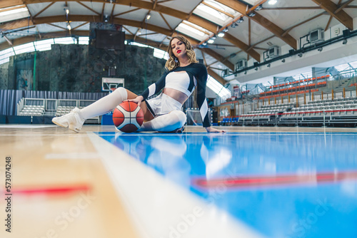 full shot of a nice-looking cheerleader with a ball sitting on the floor. High quality photo © PoppyPix