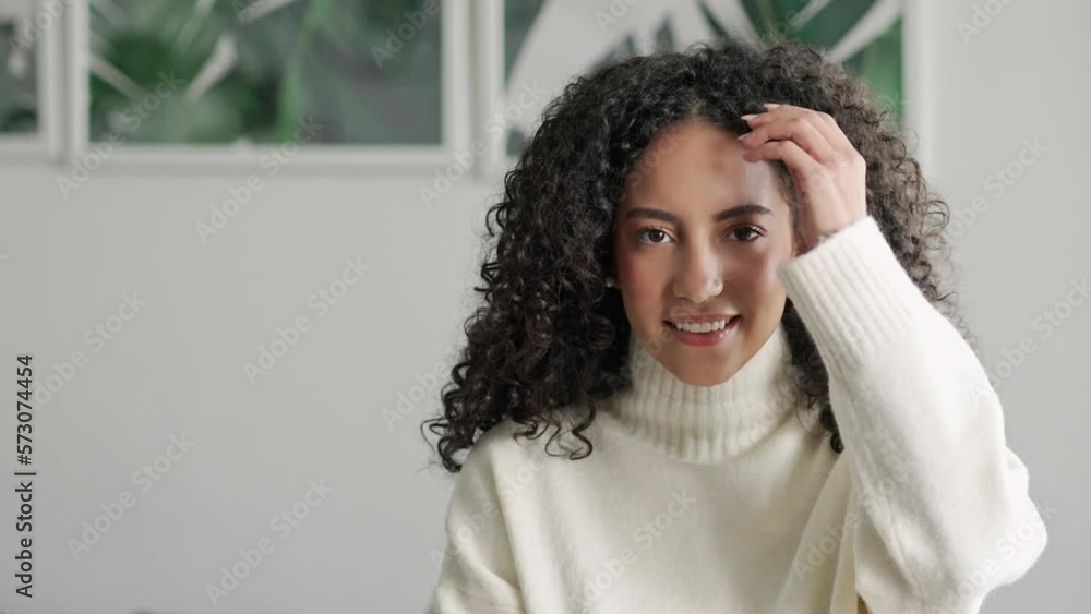 Young adult smiling pretty hispanic curly lady posing at home looking at camera, happy beautiful positive woman in modern cozy apartment living room, close up portrait. Young adult smiling pretty hispanic curly lady posing at home looking at camera, happy beautiful positive woman in modern cozy apartment living room, close up portrait.