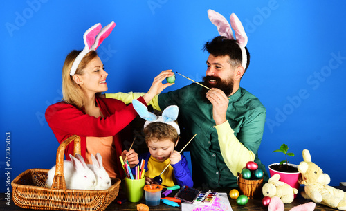 Easter family traditions. Mother, father and son painting eggs for holidays. Happy family in bunny ears painting Easter eggs together. Happy family preparing for Easter. Rabbits family on Easter.