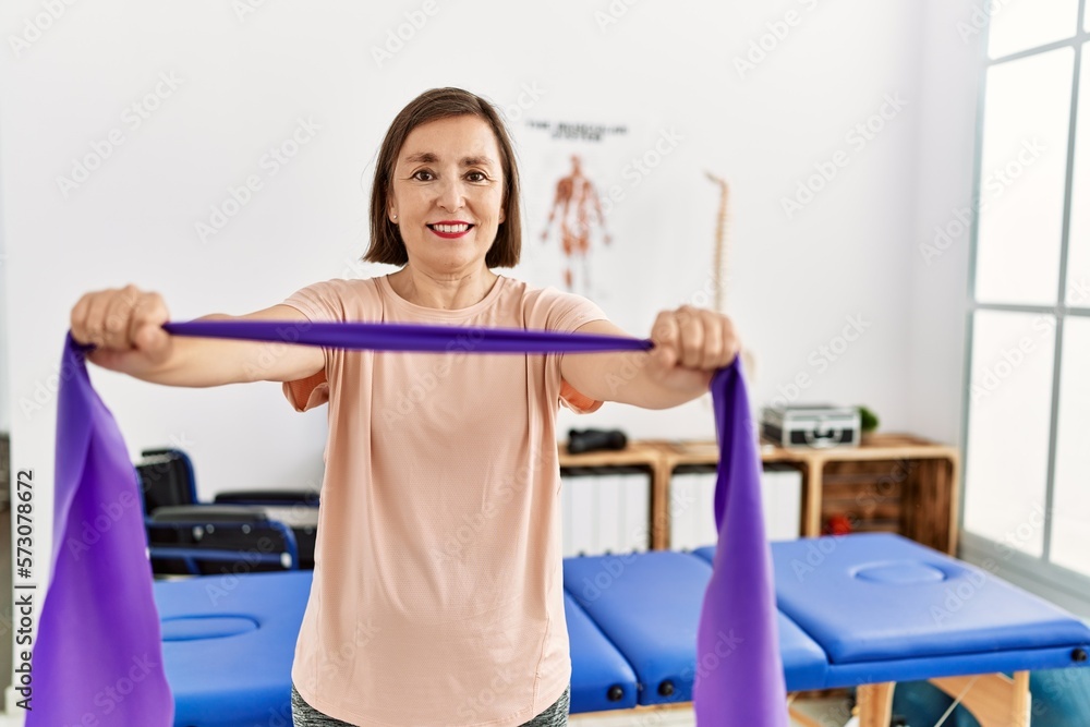 Middle age hispanic woman doing exercise with elastic bands at physiotherapy clinic