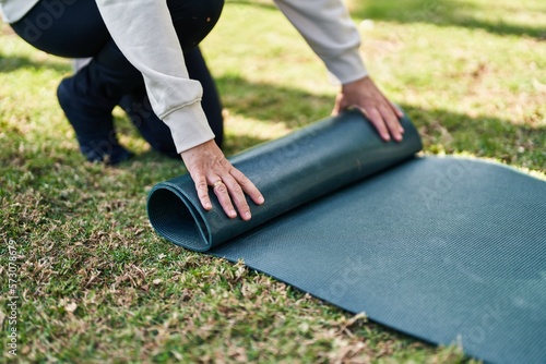 Middle age woman closing yoga mat at park