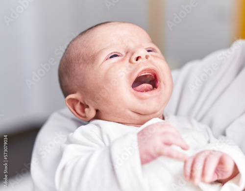 Adorable caucasian baby crying on mother arms at home