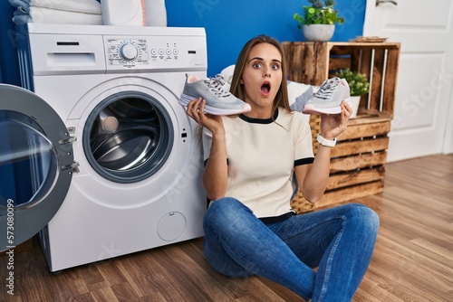 Young woman putting sneakers in washing machine afraid and shocked with surprise and amazed expression, fear and excited face.