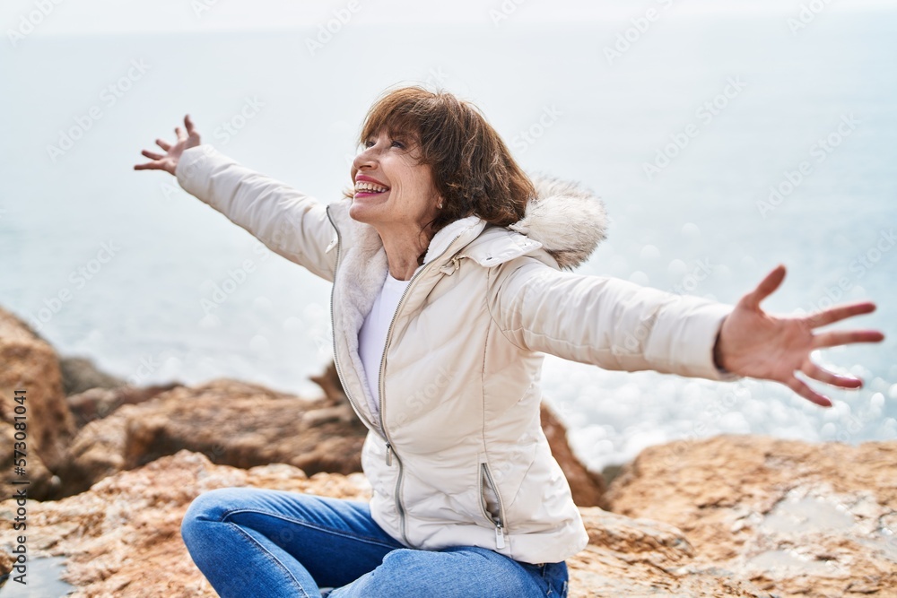 Middle age woman smiling confident sitting with arms open at seaside