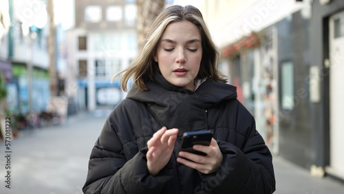 Young blonde woman using smartphone with serious expression at street