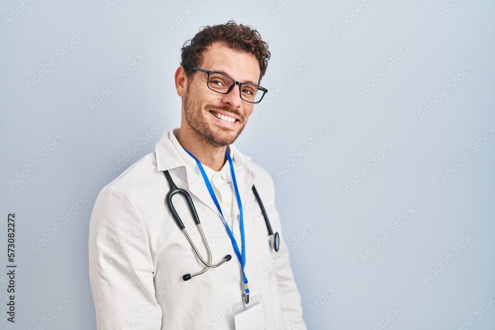 Young hispanic man wearing doctor uniform and stethoscope looking away to side with smile on face, natural expression. laughing confident. Young hispanic man wearing doctor uniform and stethoscope looking away to side with smile on face, natural expression. laughing confident.