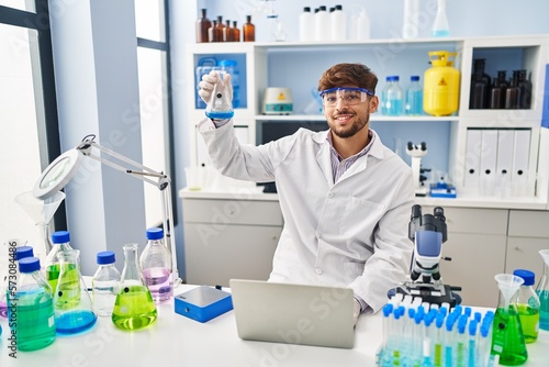 Young arab man scientist using laptop measuring liquid at laboratory