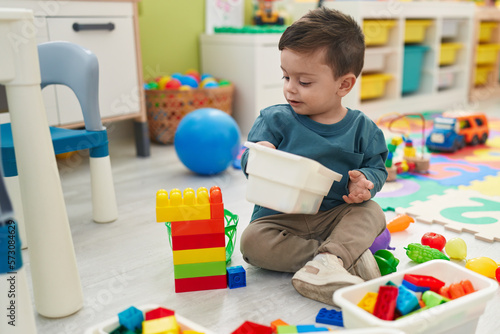 Adorable hispanic boy playing with construction blocks sitting on floor at kindergarten