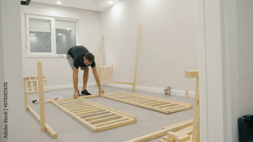Confident modern man self assembling wooden furniture placing plank on floor use screwdriver Confident modern man self assembling wooden furniture placing plank on floor use screwdriver