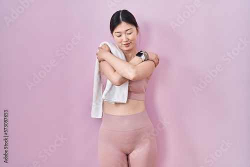 Chinese young woman wearing sportswear and towel hugging oneself happy and positive, smiling confident. self love and self care