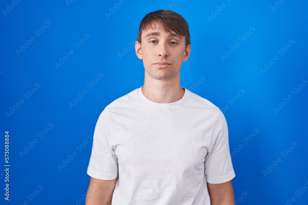 Caucasian blond man standing over blue background looking sleepy and tired, exhausted for fatigue and hangover, lazy eyes in the morning.
