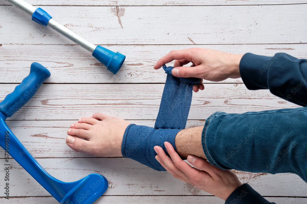 Teenage boy wrapping compression bandage around sprained ankle to