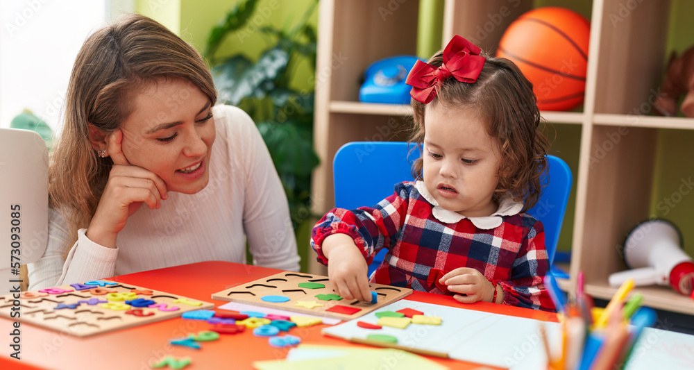 Fototapeta premium Teacher and toddler playing with maths puzzle game sitting on table at kindergarten