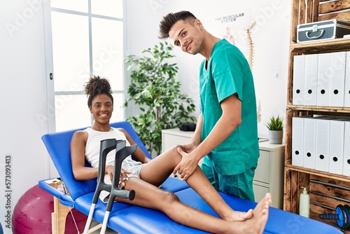Man and woman wearing physiotherapist uniform having rehab session massaging leg at physiotherapy clinic