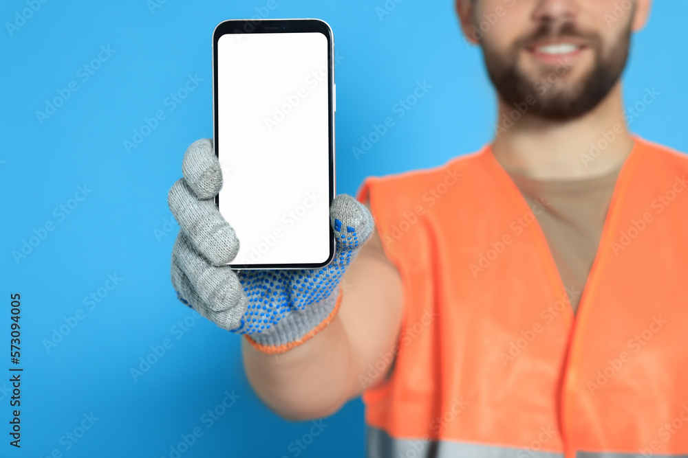 Man in reflective uniform showing smartphone on light blue background, closeup