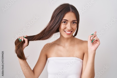 Young hispanic woman holding hair with hand smiling happy pointing with hand and finger to the side photo