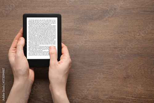 Woman using e-book reader at wooden table, top view. Space for text