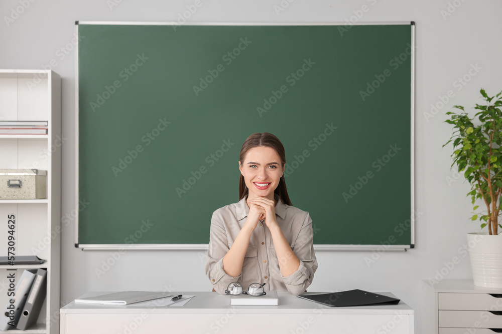 Portrait of beautiful young teacher at table in classroom Portrait of beautiful young teacher at table in classroom