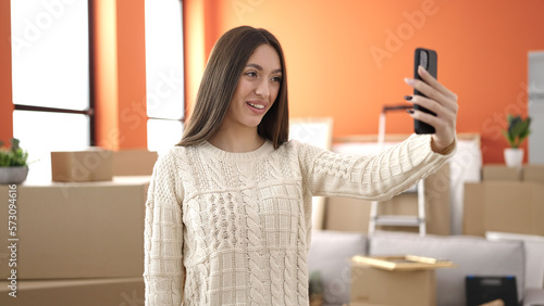 Young beautiful hispanic woman make selfie by smartphone standing at new home