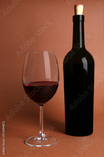Glass and bottle of red wine on brown background