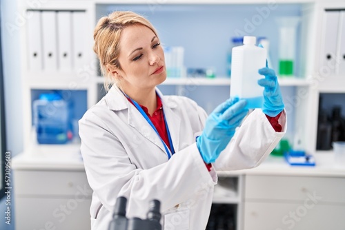 Young blonde woman scientist holding bottle at laboratory
