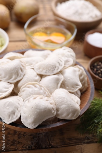 Raw dumplings (varenyky) and ingredients on wooden table, closeup
