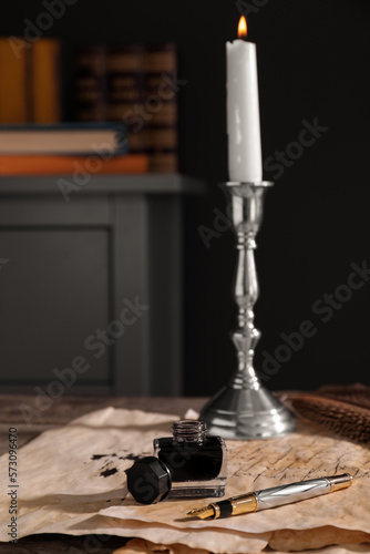 Inkwell, fountain pen, candlestick and vintage parchment with ink stains on wooden table indoors. Space for text